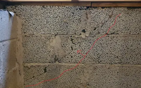 Synliga sprickor i grundmur av lättklinkerblock. En röd linje markerar en spricka som löper diagonalt över blocken.