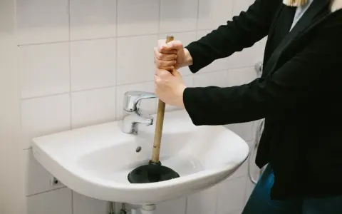 Person använder en sugpropp för att rensa vattenlås i handfatet.