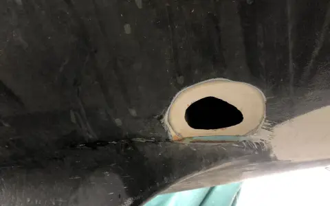 Förberedelse för att laga glasfiber. Ett hål i en mörk yta, omgivet av spackel och slipat material.