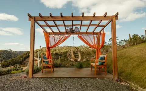 En vacker träpergola med orange draperier och hängstol. Perfekt för att bygga pergola på altan och njuta av utsikten.