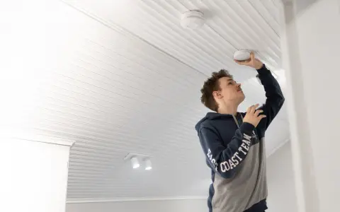 Ung man monterar en brandvarnare i taket. En viktig del av brandsäkerheten i hemmet.