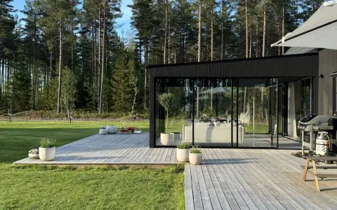 Modernt uterum med glaspartier och träaltan, perfekt för att bygga ett drömhem vid skogen.