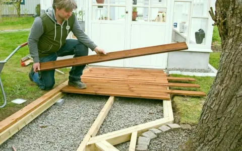 Man bygger trall vid ett växthus. Han håller en träbräda redo att läggas på plats.