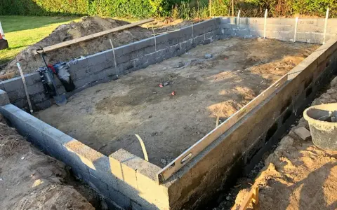 Byggarbetsplats med ett mura grund av betongblock. Schakt, spade och vattenpass syns.