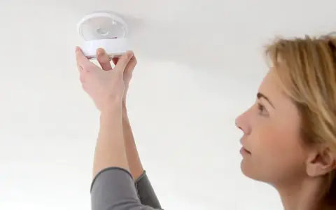 En kvinna installerar en brandvarnare. Dessa brandvarnare som pratar med varandra är viktiga för säkerheten.