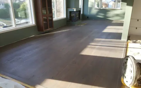 Ett rum med nylagt hårdvaxoljat golv. Solen lyser in genom fönstren och skapar vackra skuggor på det grå trägolvet.