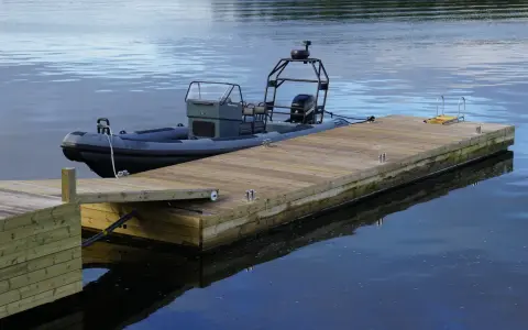 En grå RIB-båt ligger förtöjd vid en nybyggd flytbrygga i trä. Perfekt för att bygga flytbrygga och njuta av vattnet.