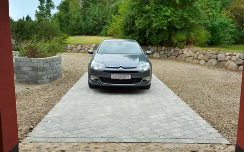 Grå bil parkerad på en vacker stenlagd uppfart. En fin uppfart inspiration med stenmur och grönska i bakgrunden.