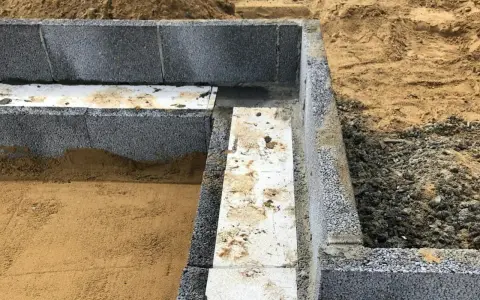 Grundläggning med lecablock, redo att putsa. Sand och grus ligger runt den påbörjade muren.