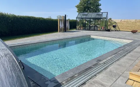 En vacker pool med mosaikdetaljer, perfekt för att bygga egen pool. Omgiven av en modern uteplats med växthus och dusch.