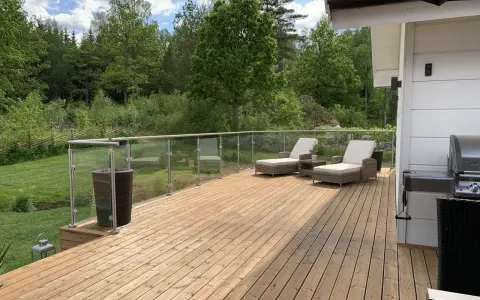Solig altan med olja trall, solstolar och grill. Vacker utsikt över grönskande skog.