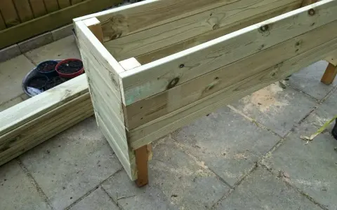 Påbörjat projekt att bygga blomlåda av tryckimpregnerat virke. Några krukor med jord står redo.