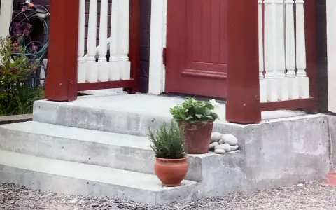 Nygjuten betongtrappa med röda stolpar och vita baluster. Krukor med växter och stenar pryder trappsteget.