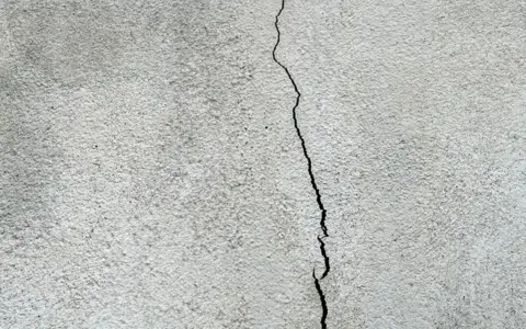 Spricka i en grå, putsad fasad. Dags att laga putsad fasad för att förhindra större skador.