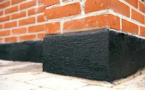 När man ska putsa sockel på ett tegelhus är det viktigt med ett bra skydd. Denna svarta, grova yta skyddar mot fukt.