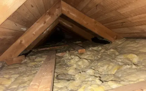 Takbjälkar och isolering i ett vindsutrymme. En del av isoleringen syns tydligt, vilket visar hur man kan isolera innertak för bättre värmeekonomi.
