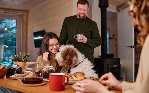 Familj med hund myser vid bordet med fika. Trots att det är lite dålig luft hemma, sprider sig värme och glädje.