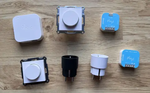 En samling Plejd-produkter, inklusive en vit Plejd-box, två dimmerknappar, två elkontakter och två styrenheter som stöder Plejd-protokoll.