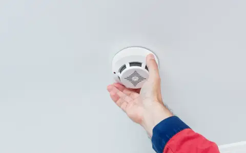 En hand monterar en brandvarnare i taket. Frågan "hur många brandvarnare ska man ha" är viktig för säkerheten.