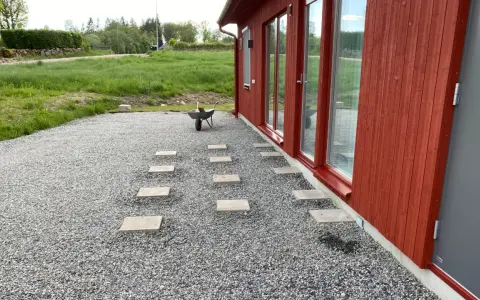 Stigande steg av altan plintar eller plattor leder genom grusgången fram till ett rött hus med stora fönster.