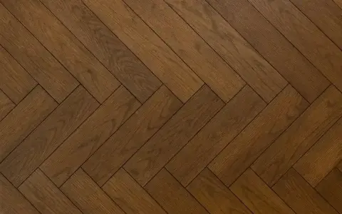 Vacker fiskbensparkett i mörkt trä, redo att slipa för att återfå sin glans.