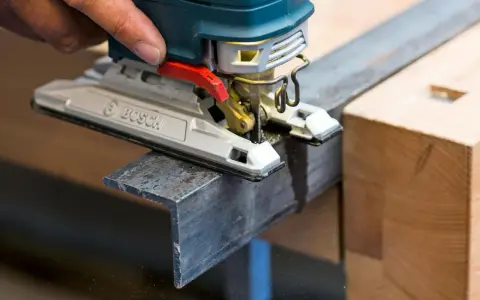 En hand använder en sticksåg för att såga snett i en metallprofil.