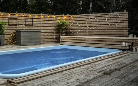 En avkopplande utomhusmiljö med pool och trädäck. En idé för att bygga eget pooltak kan inspireras av den snygga träpanelen och belysningen.