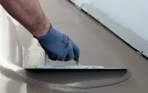 Hand med handske spacklar betonggolv med en bred spackel.