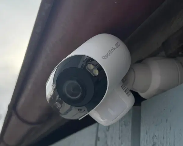 En vit Reolink Argus 4K övervakningskamera monterad under ett takutsprång.