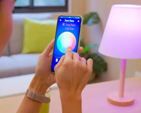Person styr lampor med iPhone. Appen "Smart Home" visar färgval för vardagsrumsljuset.