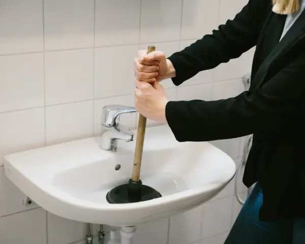 Person använder en sugpropp för att rensa vattenlås i handfatet.