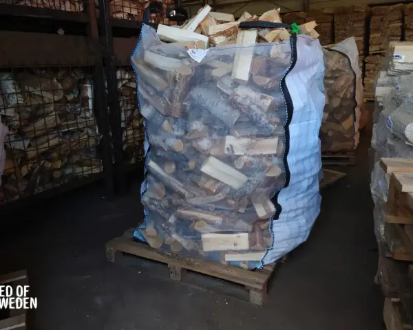 Stor säck med ved på pall, redo att stapla. Veden är kluven och förpackad för leverans.
