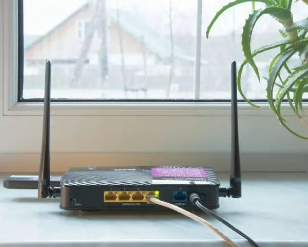 En gammal router med två antenner står på en fönsterbräda. En aloe vera-växt syns till höger.