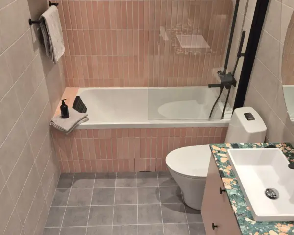 Ett modernt kaklat badrum med rosa kakel vid badkaret och grått klinkergolv. En vit toalett och ett handfat med en unik bänkskiva.