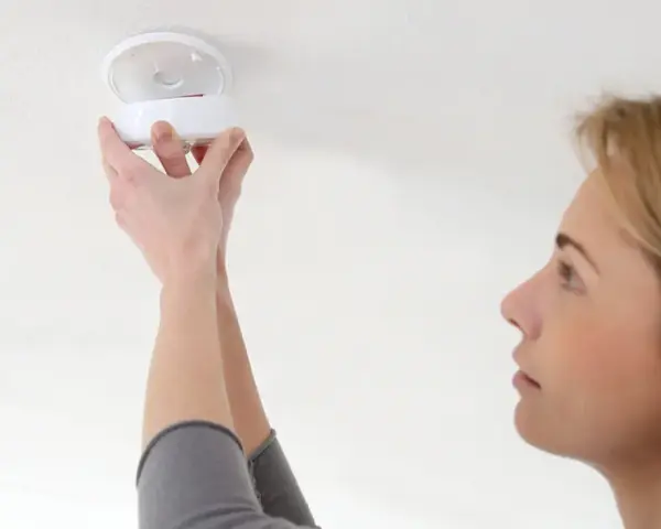 En kvinna installerar en brandvarnare. Dessa brandvarnare som pratar med varandra är viktiga för säkerheten.