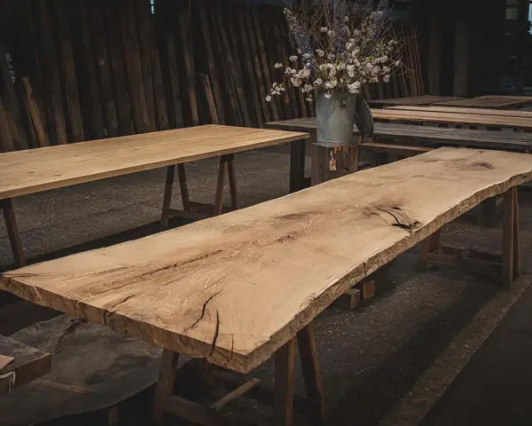 Råa ekbord med naturliga kanter, oljade och redo för utomhusbruk. En bukett blommor i en zinkhink står på ett av borden.