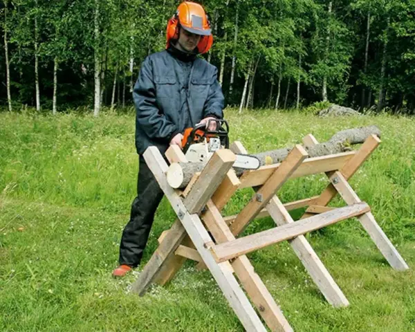 Man i skyddsutrustning använder motorsåg för att kapa ved på en sågbock. Ritning av en sådan konstruktion kan vara användbar.