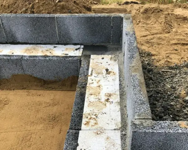 Grundläggning med lecablock, redo att putsa. Sand och grus ligger runt den påbörjade muren.