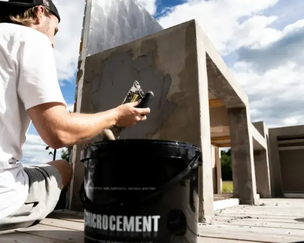 Man applicerar microcement utomhus på en betongkonstruktion. En hink med "Microcement" syns i förgrunden.