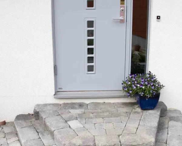 En vacker stentrappa leder upp till en modern ytterdörr. En blå kruka med blommor ger färg åt entrén.