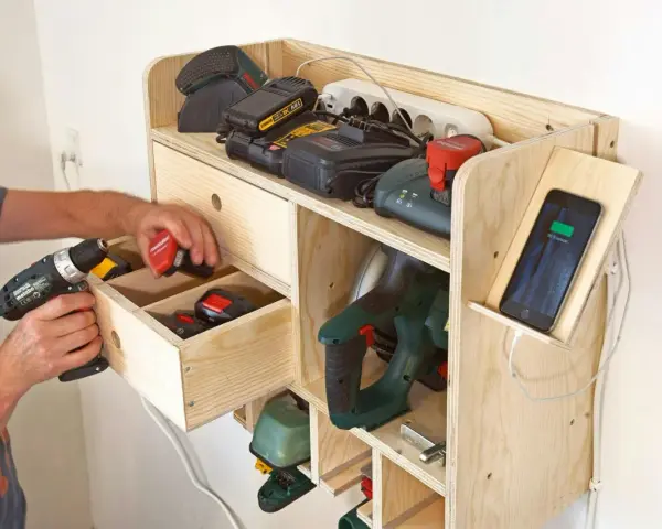 En man organiserar verktyg och batterier i en hemmabyggd laddstation. Ett bra verktyg att ha hemma för ordning och reda.