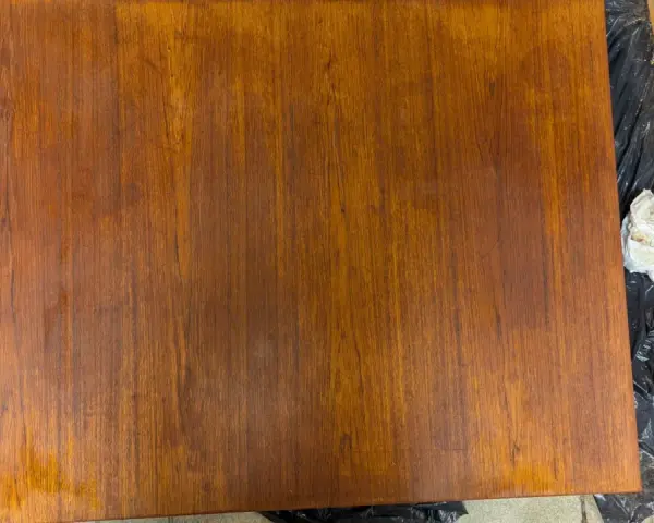 Förbereder för att slipa teakbord. En bit trä ligger på svart plast, bredvid en slipmaskin och en pappersbit.