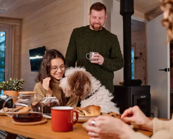 Familj med hund myser vid bordet med fika. Trots att det är lite dålig luft hemma, sprider sig värme och glädje.