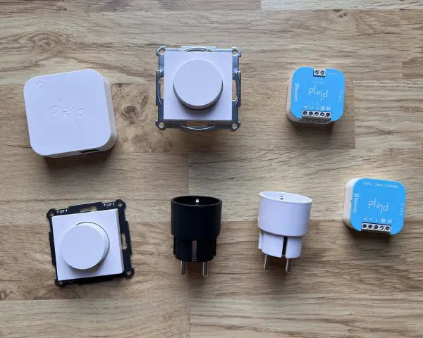 En samling Plejd-produkter, inklusive en vit Plejd-box, två dimmerknappar, två elkontakter och två styrenheter som stöder Plejd-protokoll.