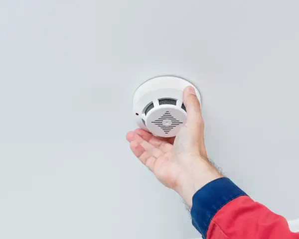 En hand monterar en brandvarnare i taket. Frågan "hur många brandvarnare ska man ha" är viktig för säkerheten.