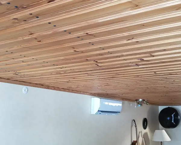 Ett vackert träpaneltak, redo att måla. En luftkonditionering och gitarrer syns nedanför.