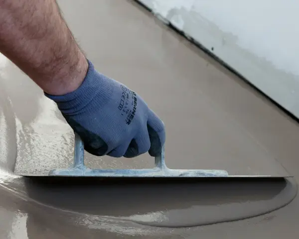 Hand med handske spacklar betonggolv med en bred spackel.