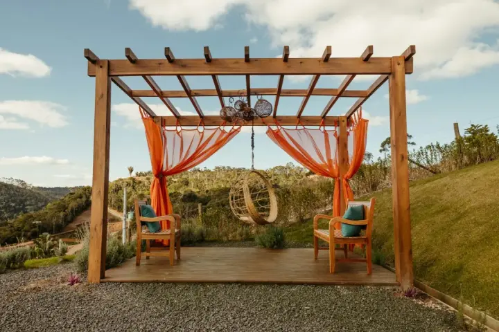 En vacker träpergola med orange draperier och hängstol. Perfekt för att bygga pergola på altan och njuta av utsikten.