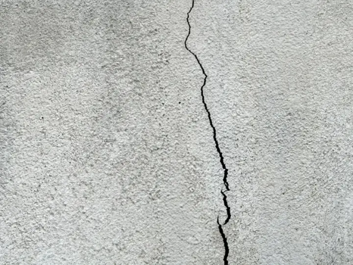 Spricka i en grå, putsad fasad. Dags att laga putsad fasad för att förhindra större skador.