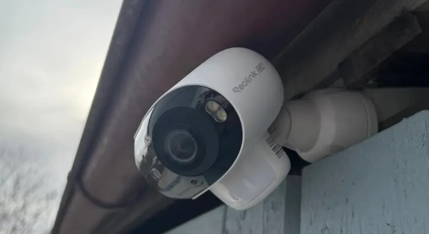 En vit Reolink Argus 4K övervakningskamera monterad under ett takutsprång.